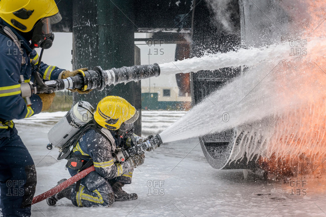 Two firemen spraying water on simulated aircraft fire at training facility