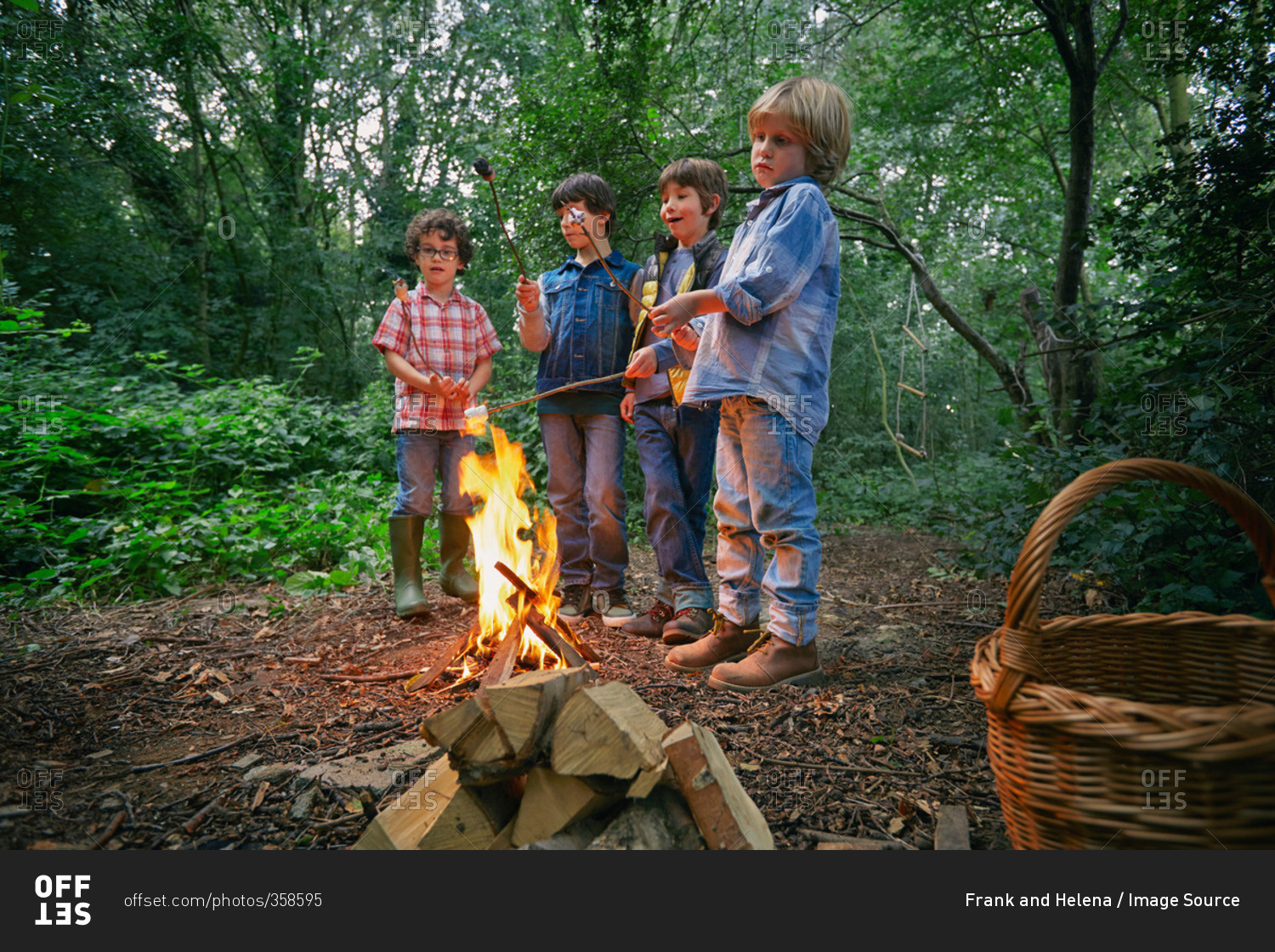 Four boys toasting marshmallows on campfire in forest