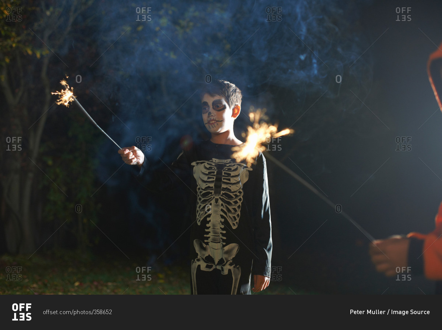 Boy wearing Halloween skeleton costume with sparkler in garden at night
