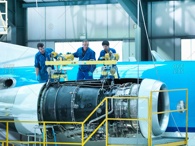 Engineers removing jet engine from aircraft in aircraft maintenance factory