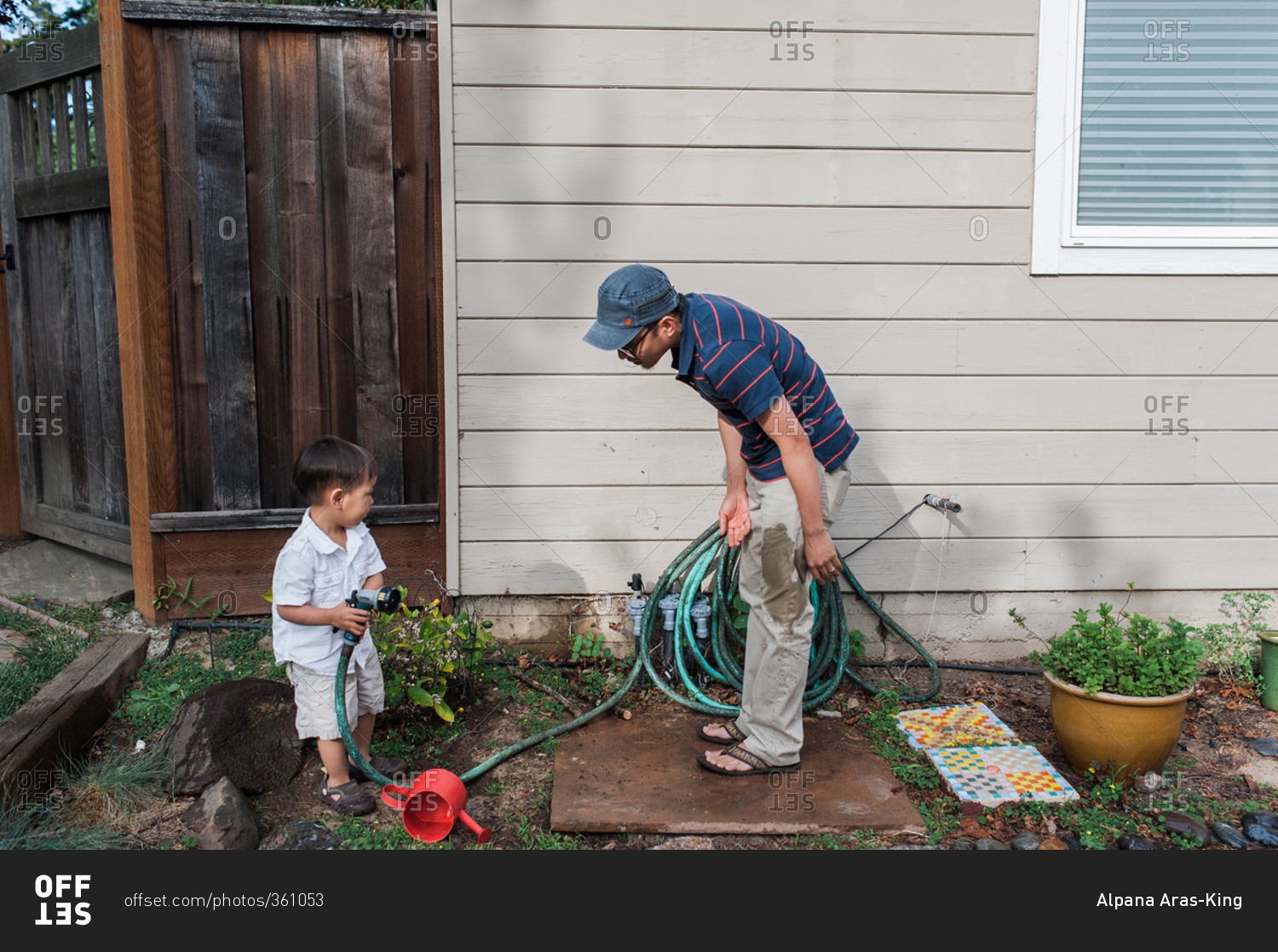 Child hold garden hose with father with wet pants