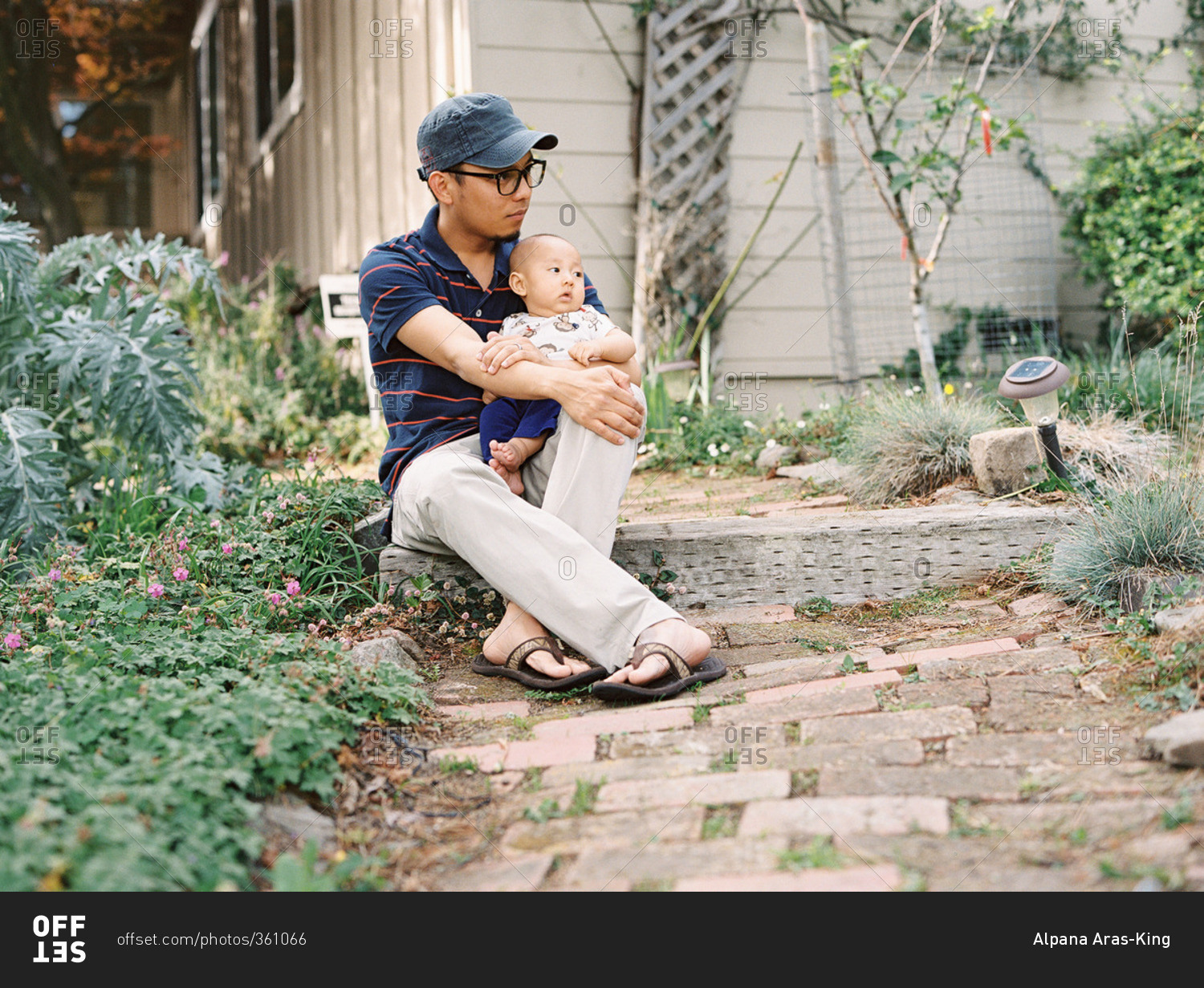 Young father in glasses and baseball hat sitting on step with his son