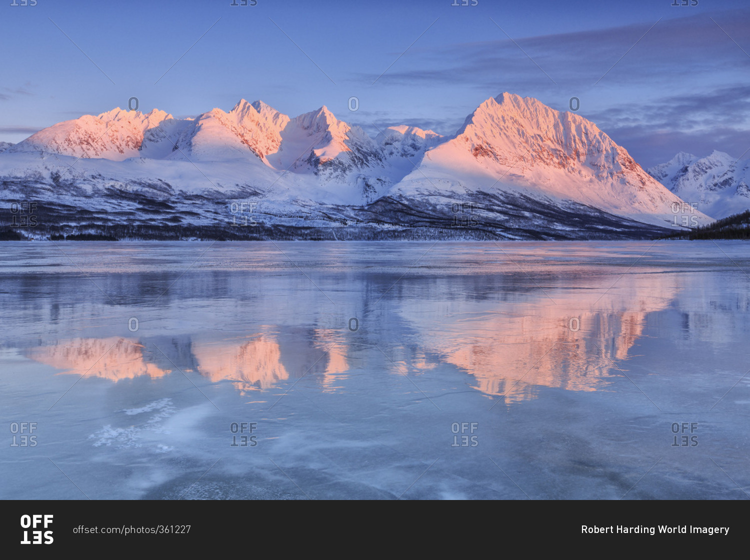 Snowy peaks are reflected in the frozen Lake Jaegervatnet at sunset Stortind Lyngen Alps Tromso Lapland Norway Europe