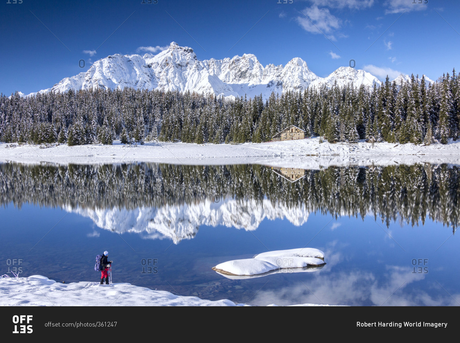 Hiker admires the snowy peaks and woods reflected in Lake Pali Malenco Valley Valtellina Lombardy Italy Europe