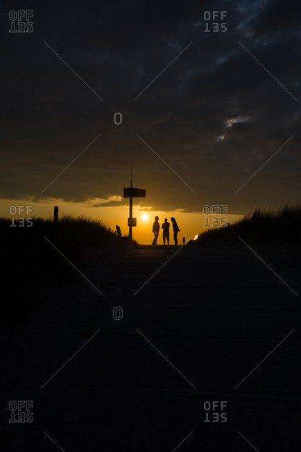 Three people standing at the entrance to the beach against the light of sunset