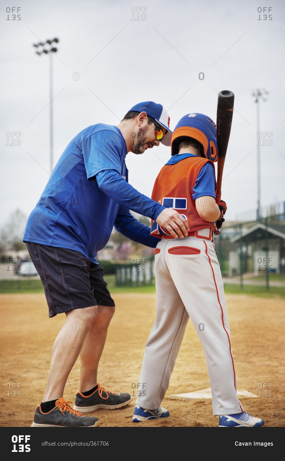 Side view of coach assisting boy in playing baseball on field