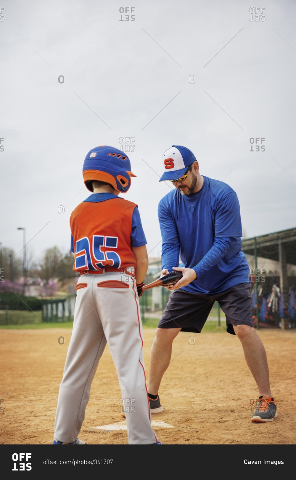 Coach assisting boy in playing baseball on field