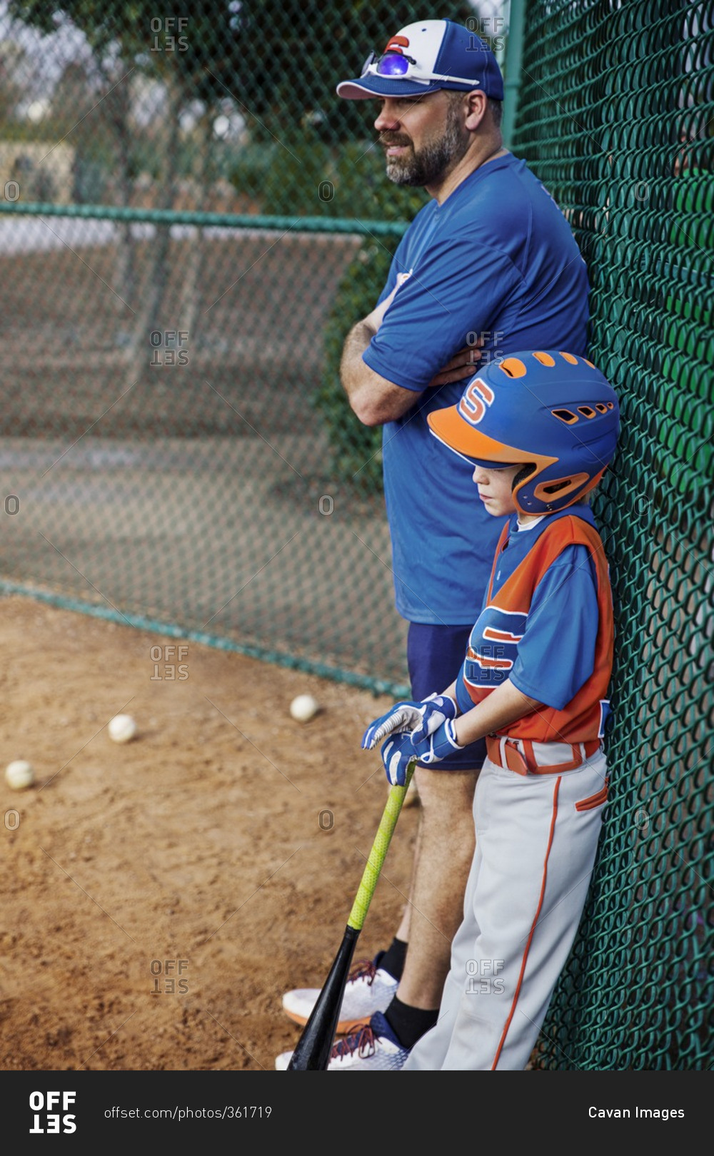 Side view of thoughtful baseball player and coach standing by chain-link fence on field