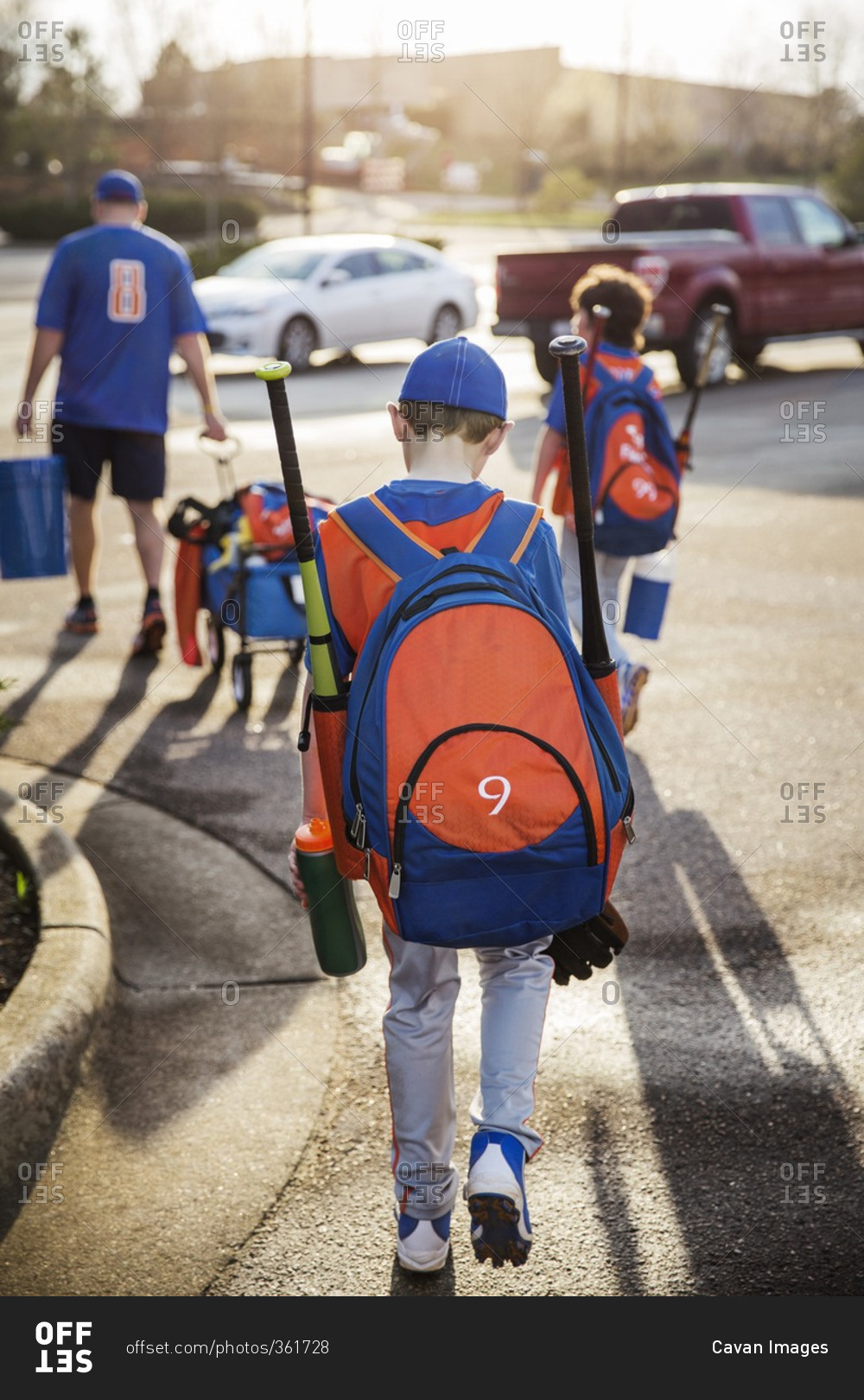 Rear view of boys and baseball coach walking on street