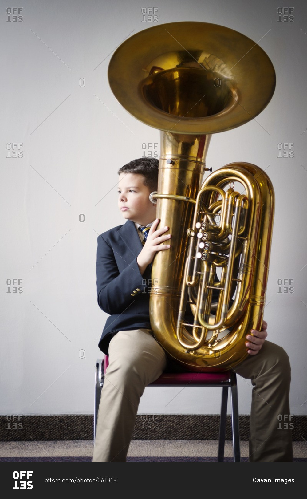 Thoughtful boy holding tuba while sitting on chair against white wall