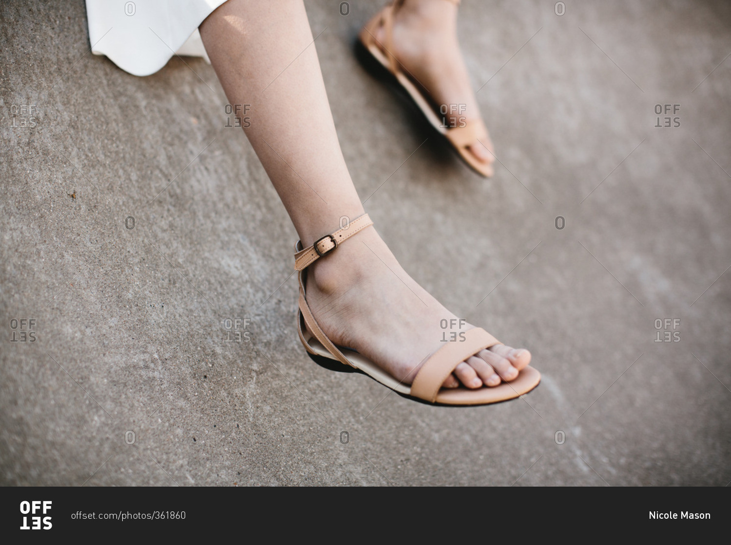 Legs of a young woman in leather sandals dangling near a cement wall ...
