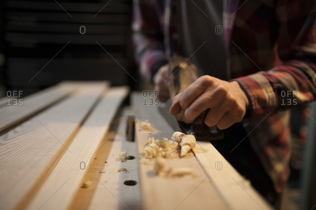 Curled wood shavings are created as a carpenter uses a hand planer to work on a piece of wood