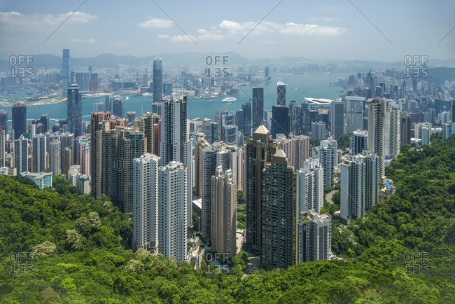 View of Victoria Harbour viewed from Victoria Peak, showing hundreds of skyscrapers nestled next to a wooded hillside; Hong Kong, China