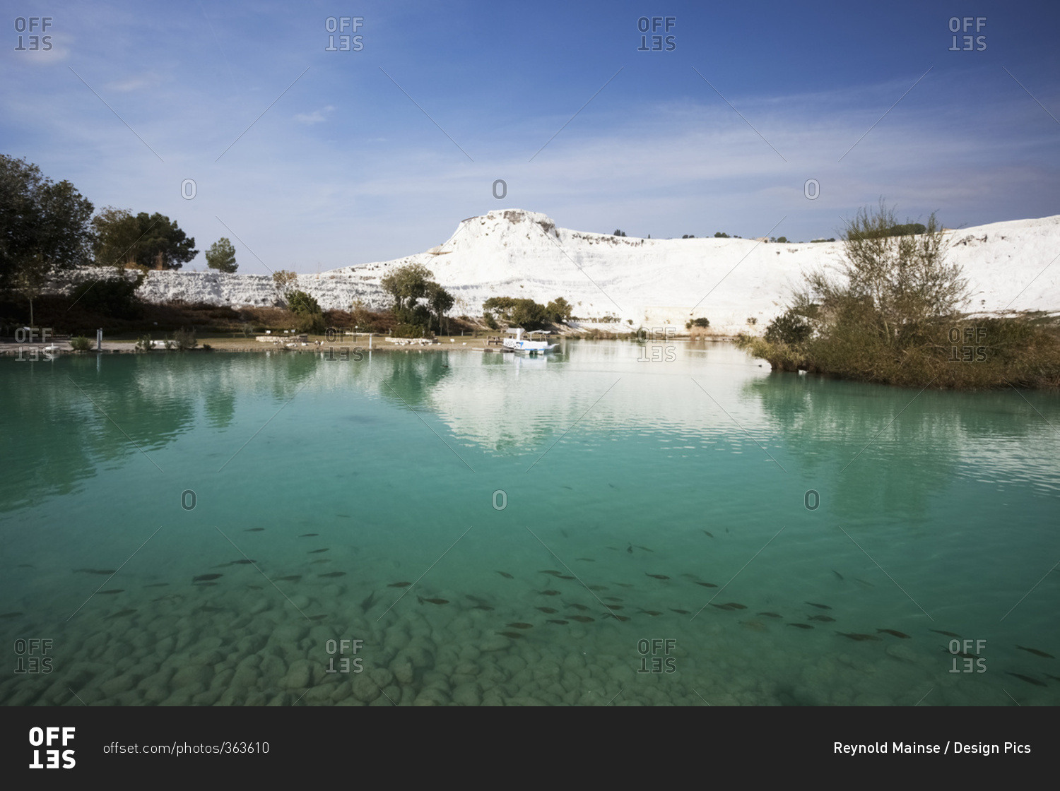 Turquoise water in a pool reflecting a white wall of mineral deposits; Pamukkale, Turkey