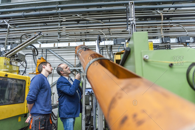 Two people in plastics factory examining a chute of a machines