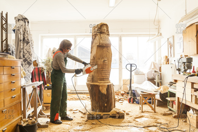 Wood carver in workshop working on sculpture with chainsaw