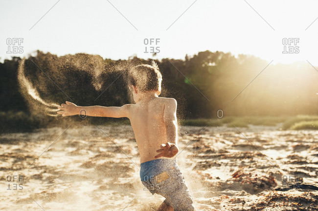 Boy running on the beach throwing sand