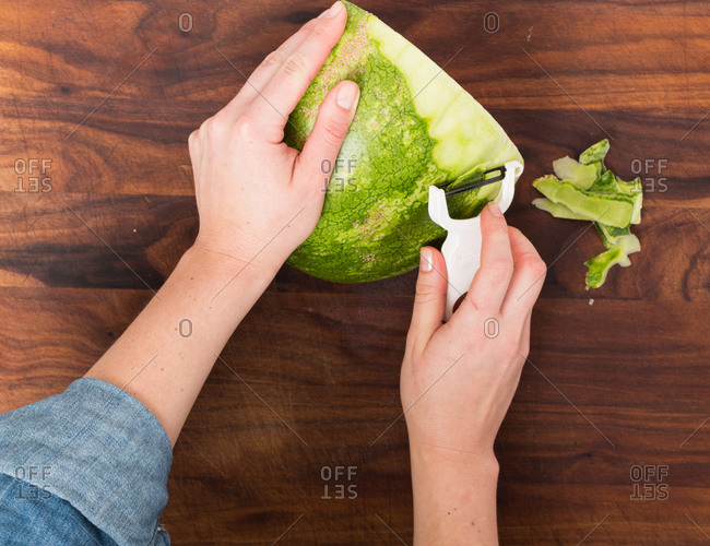 Overhead view of a person removing a watermelon rind with a hand peeler