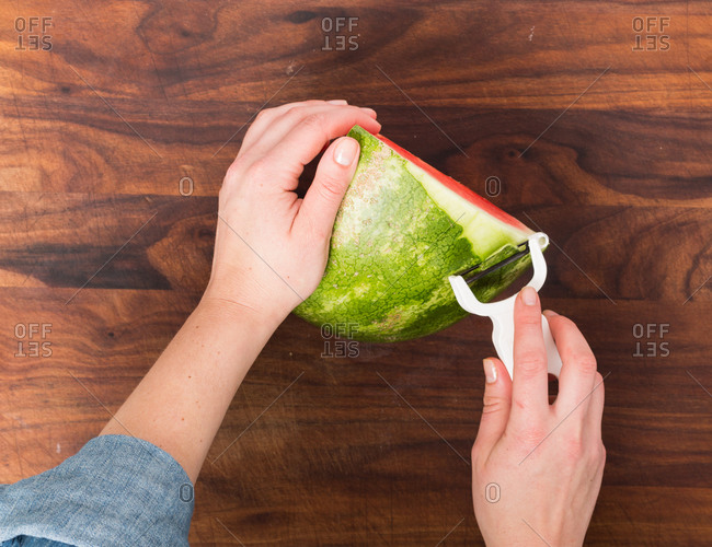 Above view of a person removing a watermelon rind with a hand peeler