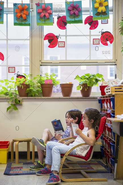 Two children reading together in classroom chairs