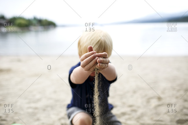 A young boy letting sand fall from between his hands