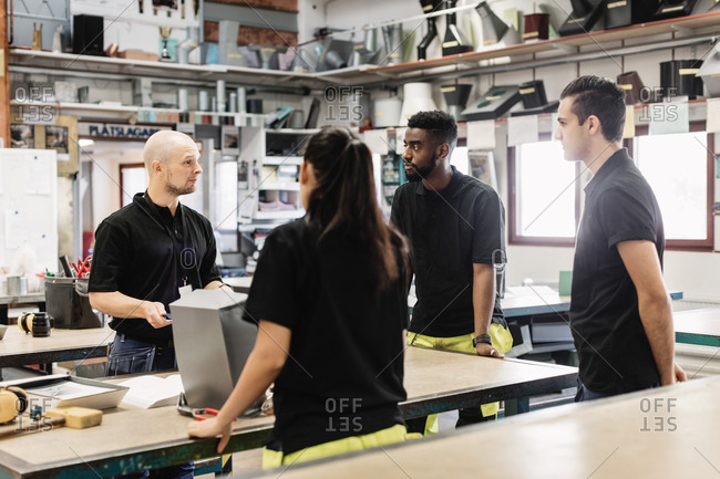 High school teacher talking with students at table in workshop