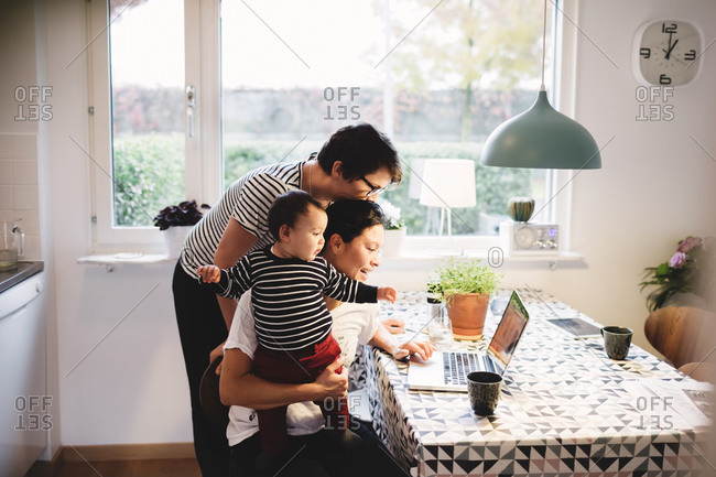 Lesbian couple with daughter looking in laptop at kitchen