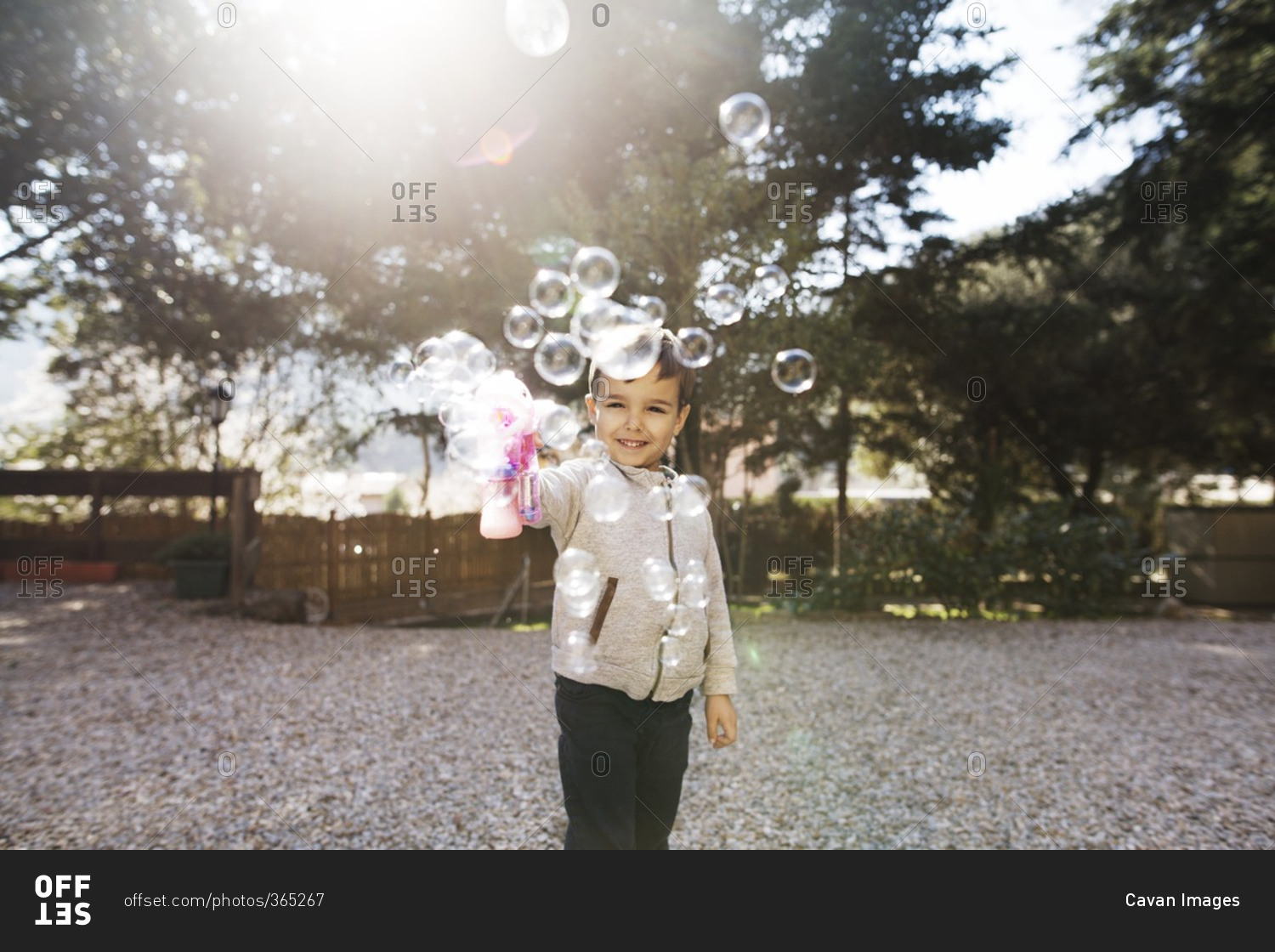 Cheerful boy playing with bubble gun at yard