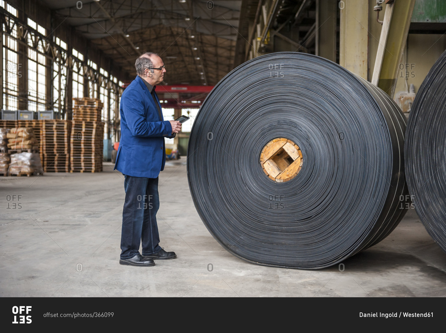 Manager with digital tablet in factory hall with rolls of rubber