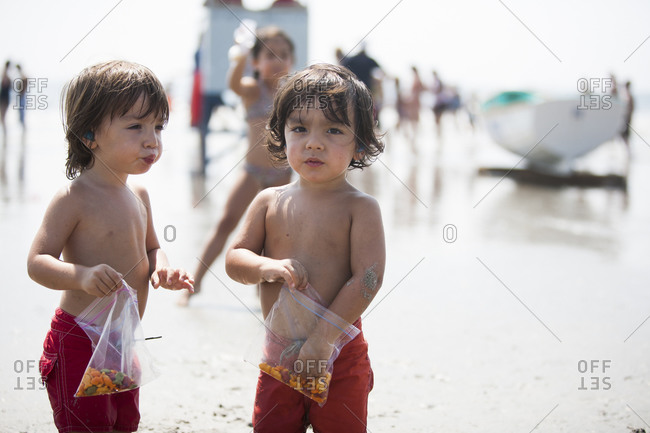 Twin toddler boys having a snack on beach