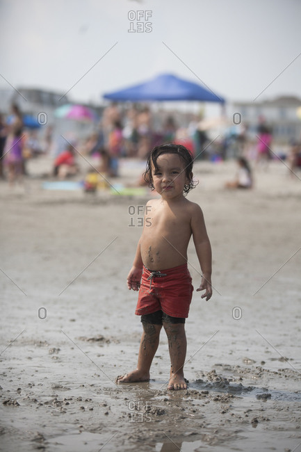 Cute toddler boy in red swim trunks on beach