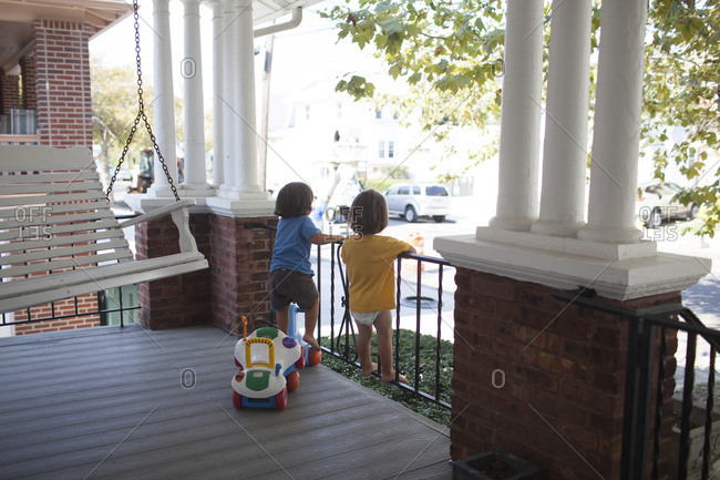Twin toddler boys standing on front porch railing