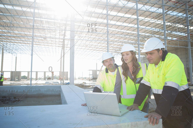 Site managers and architect looking at laptop on construction site