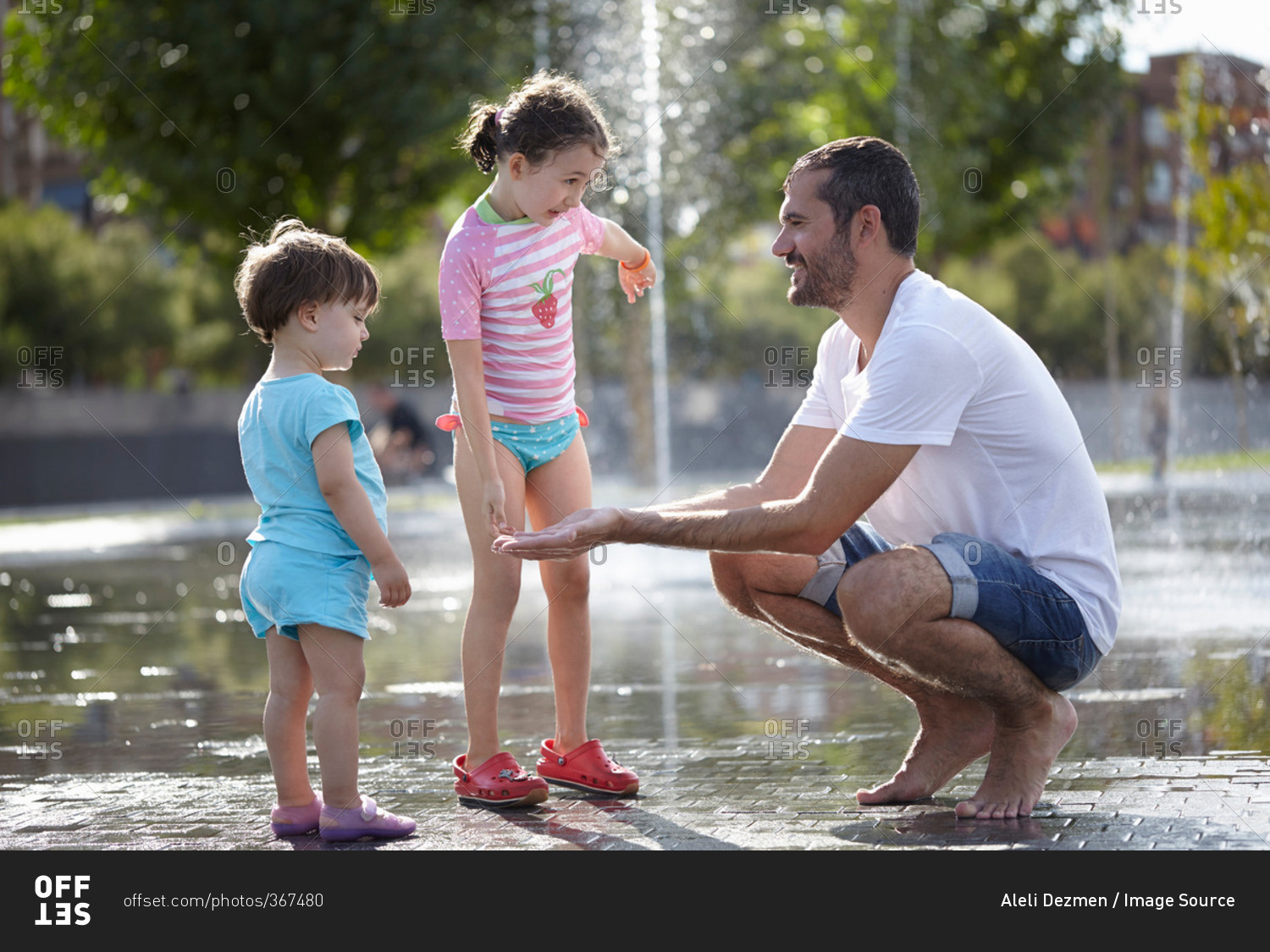 Mid adult man and two daughters playing in water fountains, Madrid, Spain