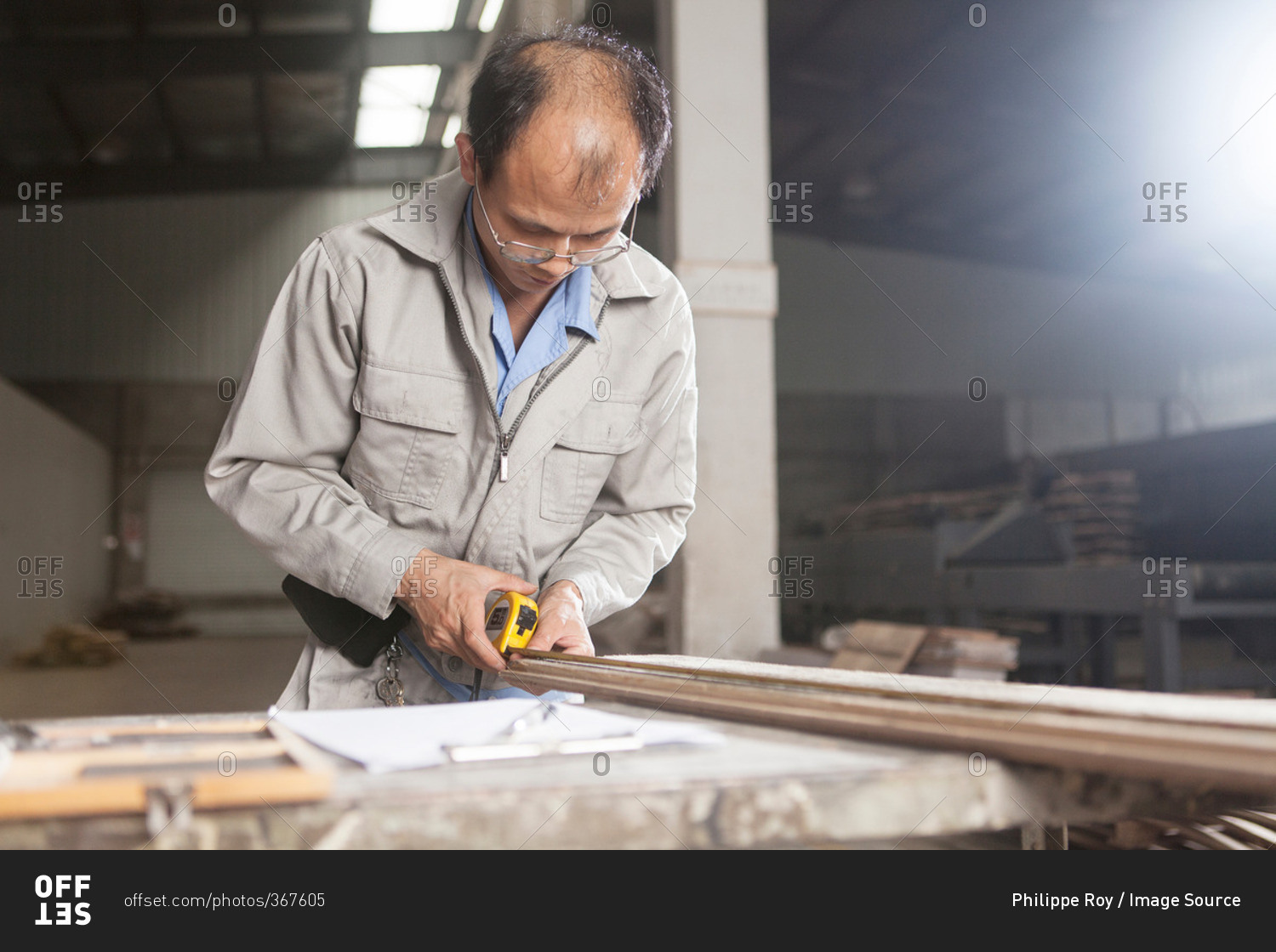 Carpenter using a tape measure to measure a wood plank with  in factory, Jiangsu, China