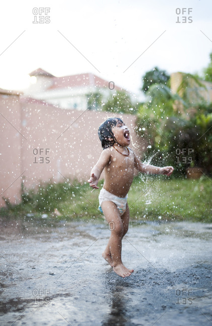 Young boy in a diaper playing outside with a water hose