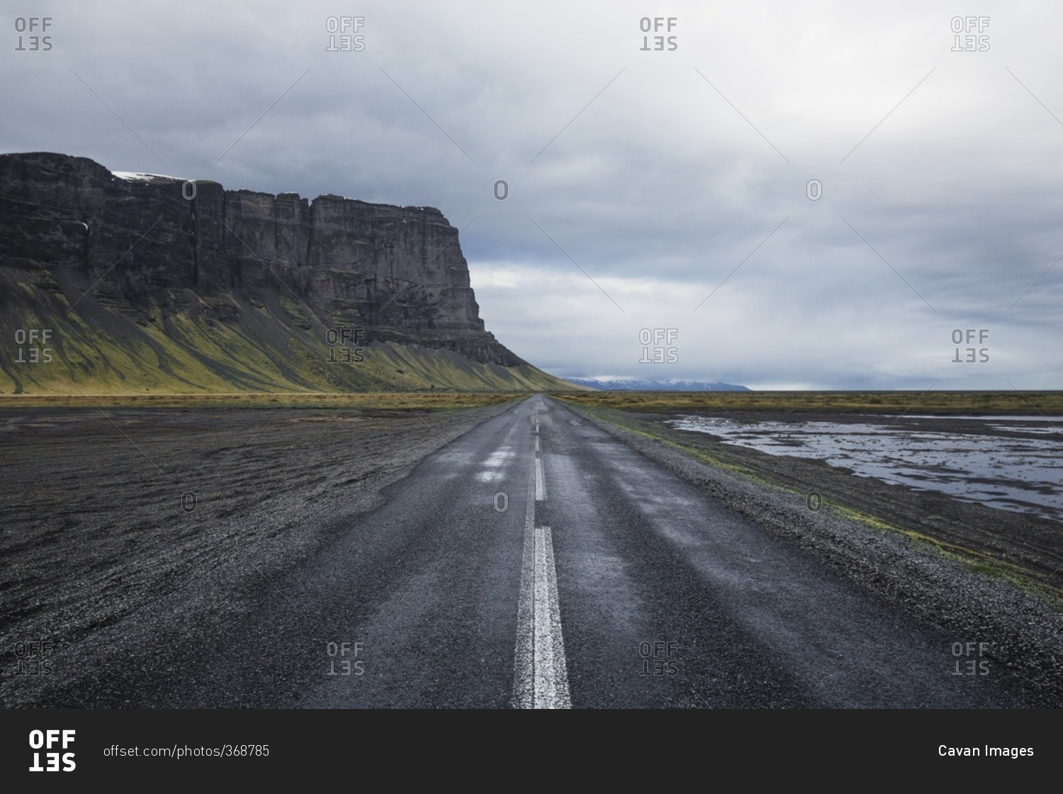 Road leading towards cliff against cloudy sky