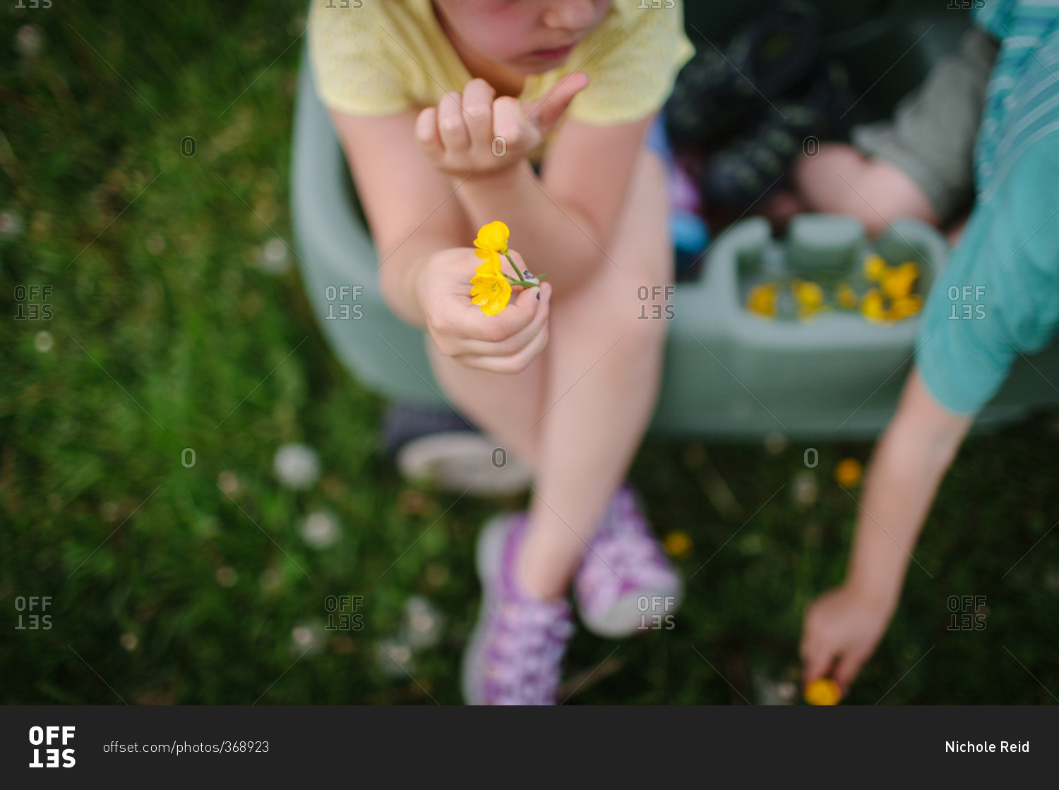 Children sitting in a green wagon holding yellow flowers
