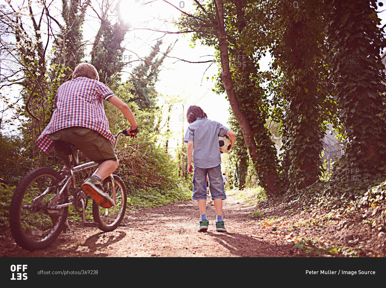 Rear view of a boy on bike with friend on forest path