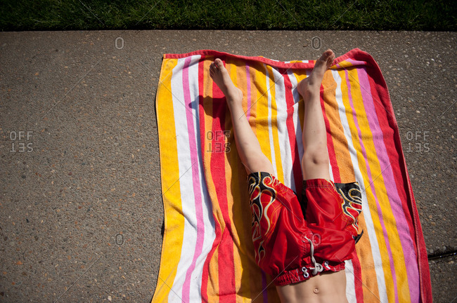 Overhead view of a boy lying down on a beach towel on the sidewalk ...