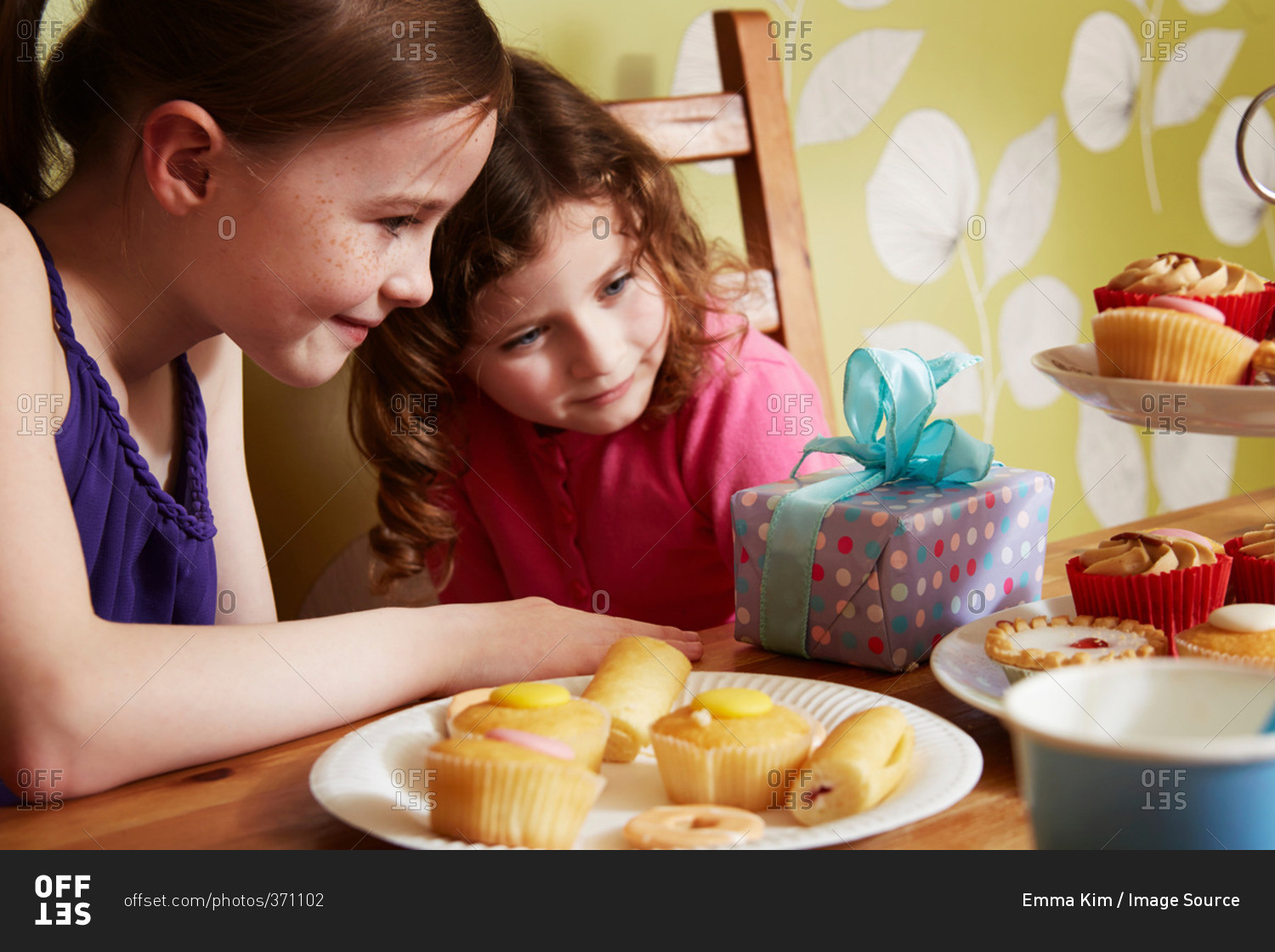 Two girls looking at birthday present with plate of cakes