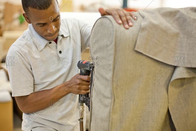 Upholsterer attaching textile to sofa using staple gun