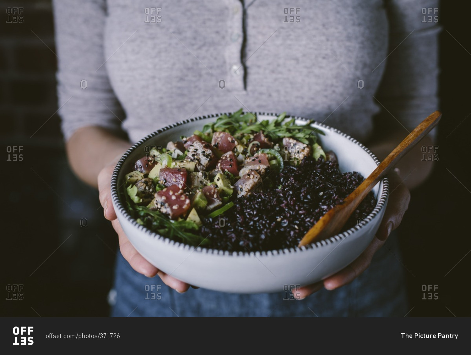 Woman holding a bowl filled with sesame crusted seared tuna salad and forbidden rice
