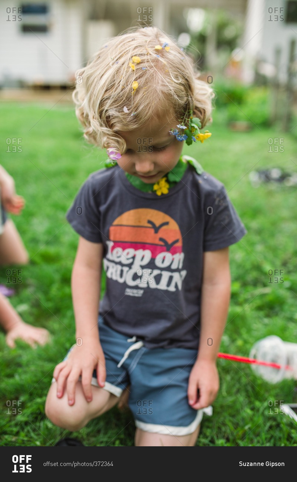 Boy with flowers in his curly blonde hair and a flower and leaves ...