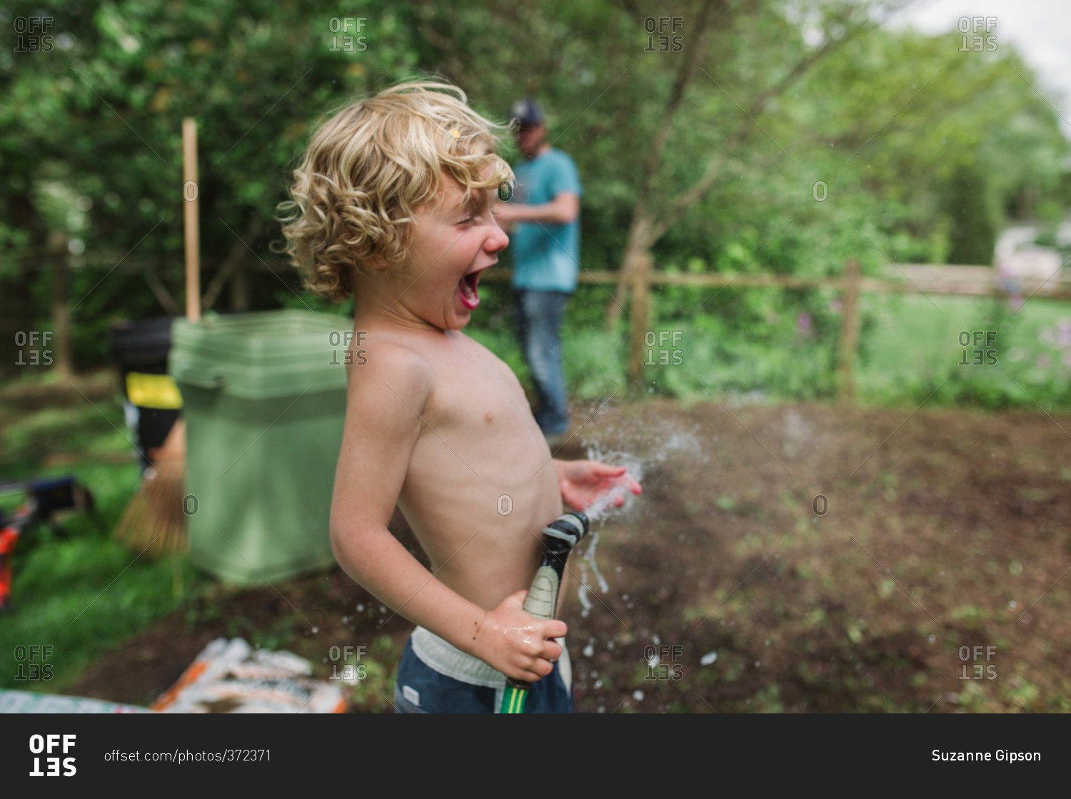 Boy standing holding a garden hose stock photo - OFFSET
