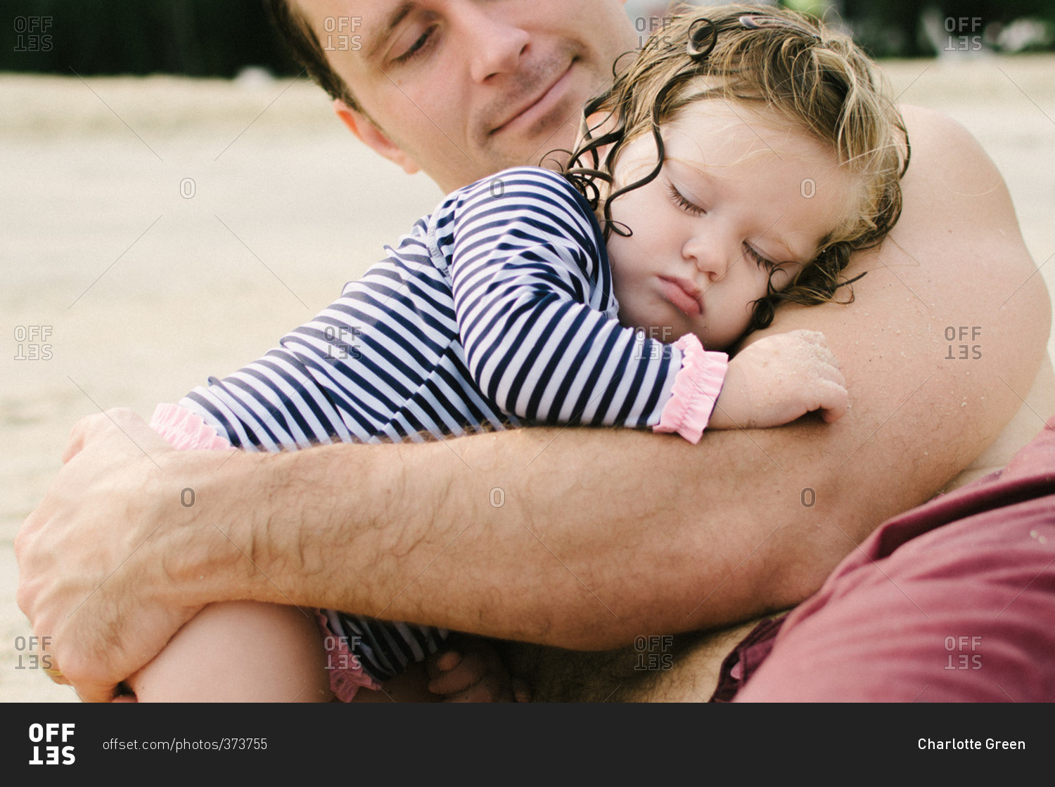 Father holding sleepy little girl on a beach