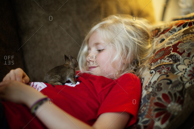 Girl cuddling on sofa with baby rodent