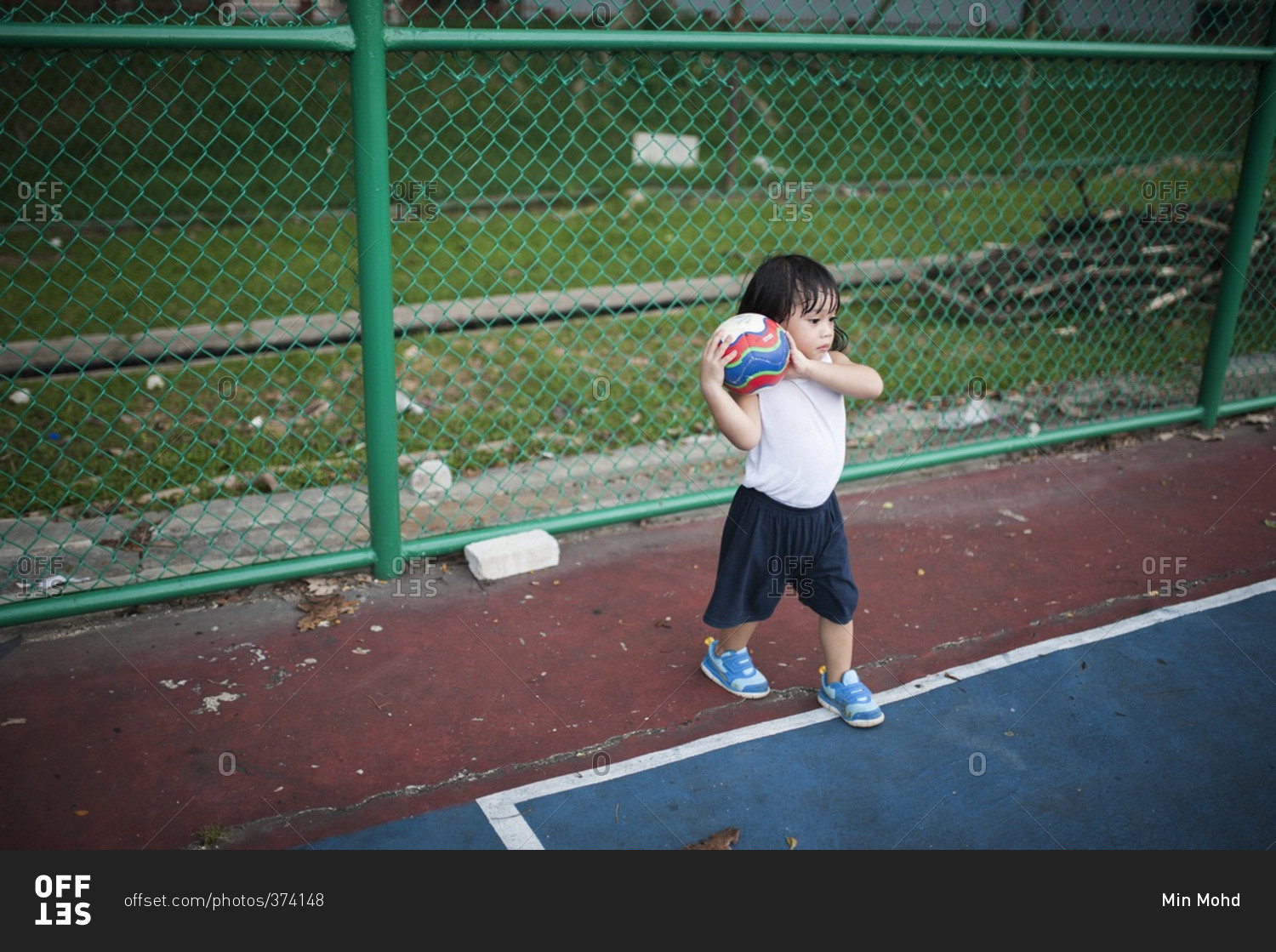 Toddler holding a soccer ball at an athletic court at a local park