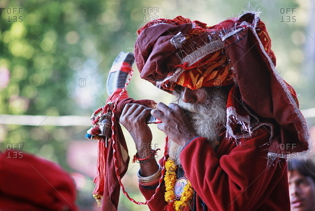 Pakistan - March 31, 2014: Senior man with a colorful head scarf blowing into a horn instrument
