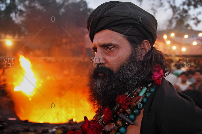 Pakistan - March 31, 2014: Man in a black turban and garland standing near a fire in a public square